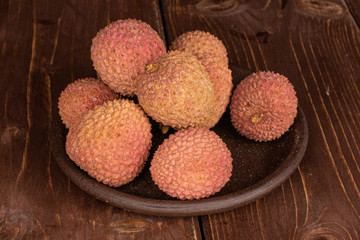 Group of seven whole fresh lychee with brown ceramic coaster on brown wood