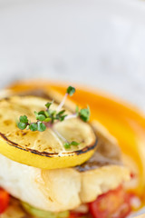 Roasted pike perch or cod fish with baked vegetables. Dish decorated with a slice of lemon. Restaurant menu