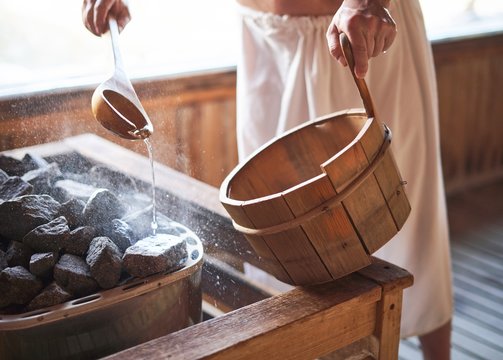 Man pouring water into hot stone in sauna room.