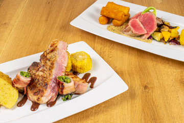 Beautiful pork neck with potato and green beans and pork tenderloin with fried potato dumplings on white rectangular ceramic plate on lacquered wood