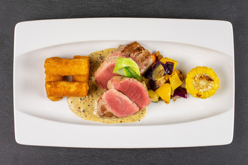Beautiful pork tenderloin with fried potato dumplings on white rectangular ceramic plate flatlay on grey stone