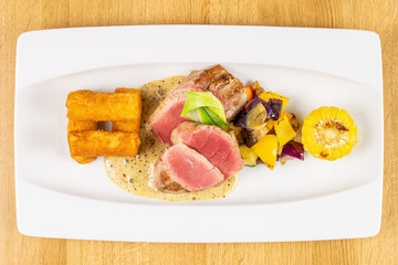 Beautiful pork tenderloin with fried potato dumplings on white rectangular ceramic plate flatlay on lacquered wood