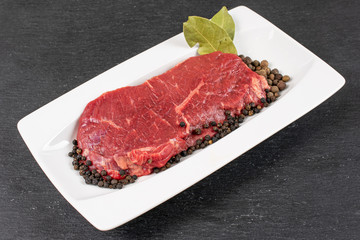 Beautiful raw beef sirloin with spices on white rectangular ceramic plate on grey stone