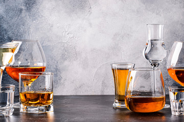 Set of strong alcoholic drinks in glasses in assortment: vodka, cognac, tequila, brandy and whiskey, grappa, liqueur, vermouth, tincture, rum. Gray bar counter background, copy space