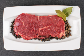 Beautiful raw beef sirloin with spices on white rectangular ceramic plate flatlay on grey stone
