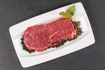 Beautiful raw beef sirloin with spices on white rectangular ceramic plate flatlay on grey stone