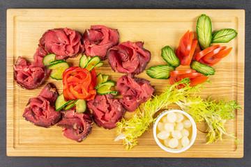 Beautiful sliced roast beef with pickled onions on wooden cutting board flatlay on grey stone