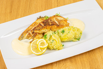 Beautiful zander with smashed potatoes on white rectangular ceramic plate on lacquered wood