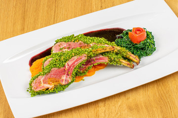 Beautiful veal ribs with sweet potatoes puree and spinach and dark sauce on white rectangular ceramic plate on lacquered wood