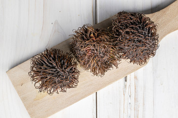 Group of three whole old brown rambutan on wooden cutting board flatlay on white wood