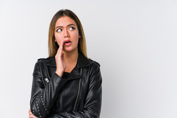 Young caucasian woman wearing a black leather jacket is saying a secret hot braking news and looking aside