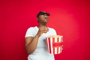 Emotional watching cinema. African-american young woman's portrait on red background. Beautiful female model. Concept of human emotions, facial expression, sales, ad, inclusion, diversity. Copyspace.