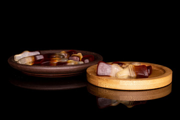 Lot of whole sweet jelly cola with brown ceramic coaster on round bamboo coaster isolated on black glass