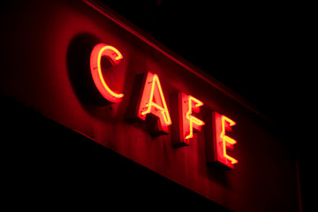 Red neon sign with open tubes shining in the dark, forming the word "CAFE" 