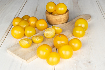 Group of lot of whole four halves of fresh yellow tomato on wooden cutting board in bamboo bowl on white wood