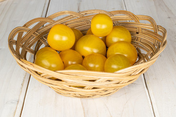 Lot of whole fresh yellow tomato in round rattan bowl on white wood