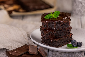 A stack of chocolate brownies on wooden background with mint leaf on top, homemade bakery and dessert