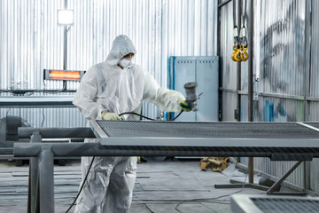 A paint shop worker with industrial sprayers in his hands.