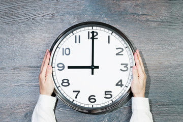 Hands of woman in business suit hold big plain wall clock on rusitc wood background. Nine oclock....