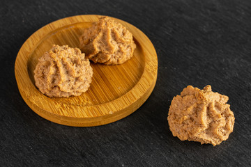 Group of three whole homemade brown coconut biscuit with chocolate on bamboo coaster on grey stone