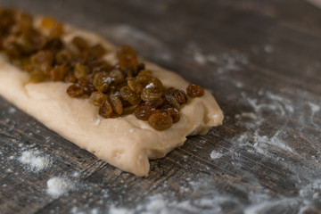 Fresh homemade dough sliced with raisins on a wooden table. Wheat flour is scattered on the table. The process of making pies.