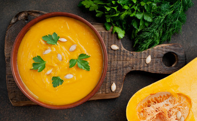 pumpkin cream soup with seeds and herbs on a stone background. healthy food.