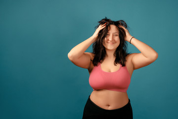 Fototapeta premium Happy plus size positive woman. Happy body positive concept. I love my body. Attractive overweight woman posing on camera in the studio on a colored background. Girl is wearing a coral bra