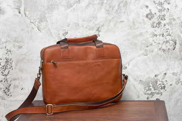 Leather business bag and accessories in the work room with gray concrete wall, wood table and...