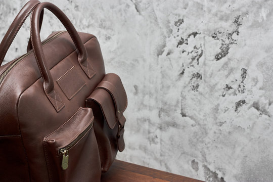 Leather Business Bag And Accessories In The Work Room With Gray Concrete Wall, Wood Table And Leather Chair.