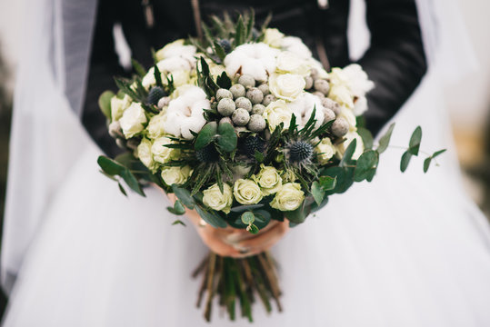 Wedding bouquet in the hands of the bride. Khimki bouquet with white roses, cotton, thorns and greenery