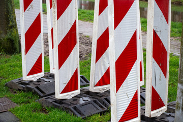 Fototapeta na wymiar Red & white reflective roadblock barricades for directing traffic during road work or maintenance in a construction zone. Concept of traffic safety or road traffic.