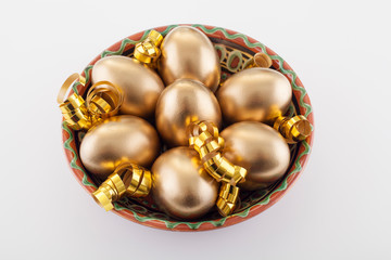 Obraz na płótnie Canvas Golden eggs in a plate, on a white background, decorated with gold ribbons, next to the place for text. The concept of Passover and the holiday symbol.
