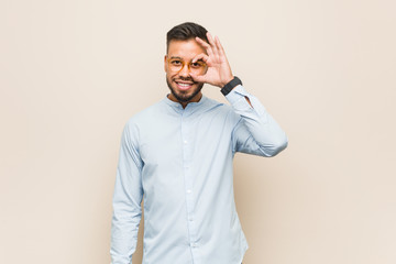 Young south-asian business man excited keeping ok gesture on eye.
