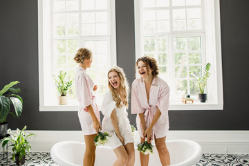 young beautiful blonde wedding bride in a beautiful white dress having fun with bridesmaids in the bathroom