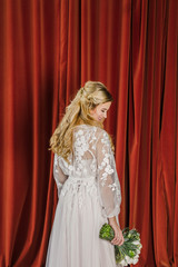 young beautiful blonde wedding bride in a beautiful white dress stands on a red background