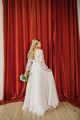 young beautiful blonde wedding bride in a beautiful white dress stands on a red background