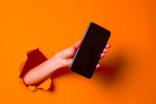 A Woman Holds A Phone Through Ragged Orange Paper Background, Close-up.