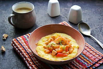 Homemade shrimp and grits with smoked sausages, sweet red peppers, onions and cheese in a pink bowl on a dark concrete background. American cuisine. Recipes with corn grits.