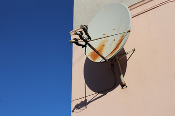 A round satellite dish on the corner of a building against a blue sky. TV antenna on the wall of a building