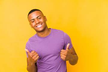 Young latin man isolated on yellow background raising both thumbs up, smiling and confident.