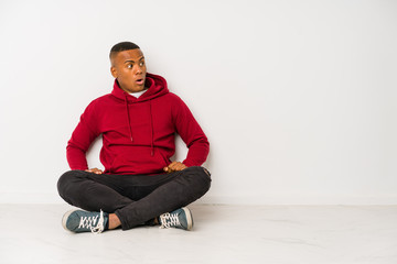 Young latin man sitting on the floor isolated being shocked because of something she has seen.