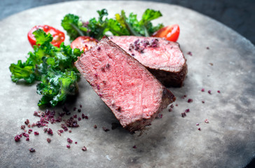 Barbecue dry aged wagyu roast beef natural sliced offered with rapini and tomatos as closeup on a modern design plate