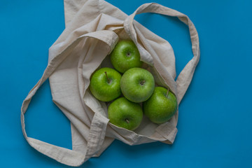 Eco friendly friend's bag for linen products with beautiful green apples on a blue background against a plastic bag.