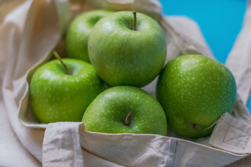 Eco friendly friend's bag for linen products with beautiful green apples on a blue background against a plastic bag.