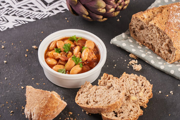 Baked beans in tomato sauce on black stoneware with bread, meal.