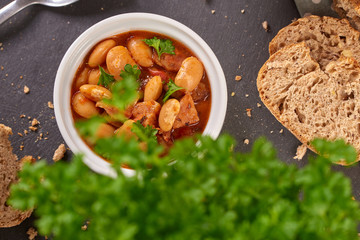 Baked beans in tomato sauce on black stoneware with bread, meal.