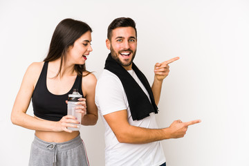 Young caucasian fitness couple isolated excited pointing with forefingers away.