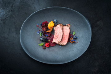 Gegrilltes dry aged Wagyu Roastbeef natur aufgeschnitten mit Gemüse Chips und Waldbeeren als Draufsicht auf einem Modern Design Teller mit Textfreiraum