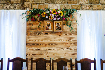 Decorations made of wood and wildflowers served on the festive table setting in rustic style for wedding ceremony. Wooden stage, wall on the restaurant for party.