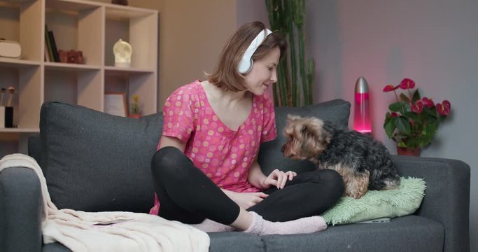 Woman listening yo music on smart phone, moving to the rythm while sitting on sofa.